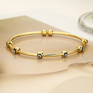 Detalle de la pulsera rígida dorada con cuentas de ojo turco en esmalte sobre fondo beige