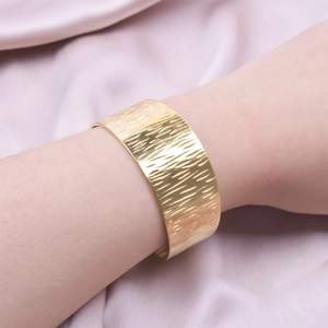 Polished gold wide striped C-shaped cuff bracelet worn on wrist over silk background
