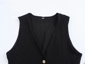 Detail of black textured V-neck vest top featuring subtle pleats and a single button
