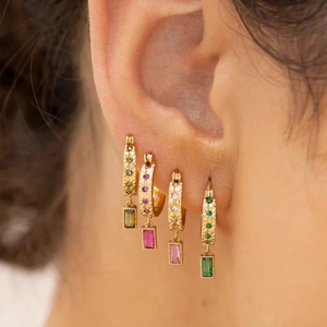 Macro shot of gold hoop earrings with colorful emerald-cut stones on a model's ear