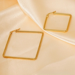 Detail view of large square gold titanium steel hoop earrings on champagne silk fabric