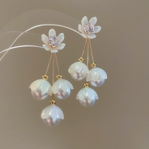 Détails de boucles d'oreilles muguet avec pétales blancs et pampilles dorées