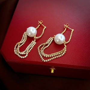 Detail of elegant gold-toned earrings featuring large white pearls and rhinestone tassels