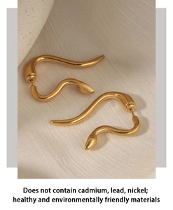 Close-up of golden snake-shaped 316L stainless steel earrings on beige fabric background
