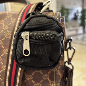 Detail of a black nylon mini coin purse with silver zipper attached to a striped strap