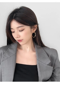 Close-up of elegant gold twisted geometric hoop earrings worn by a model in grey suit