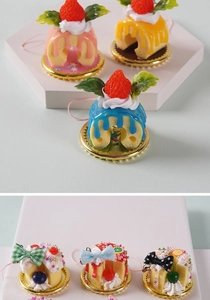 Detalle de colgantes mini postres con crema, fresa y base dorada para bolsos y móvil
