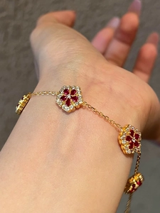 Detailed close-up of a gold-plated bracelet with red gemstone flower charms on wrist