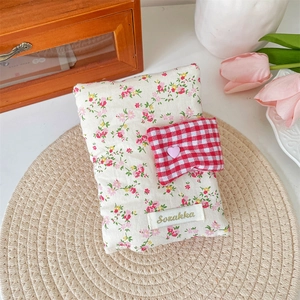 Detailed shot of a floral fabric book cover with a red checkered pocket and pink heart charm