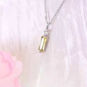 Detail of silver necklace with rectangular yellow zircon pendant on soft fabric with flowers