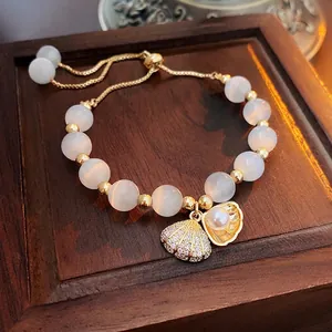 Gold-plated cat eye stone and pearl bracelet with shell charm on wooden stand