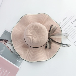 Flat lay of pink straw sun hat with black mesh bow and polka dot ribbon on magazines