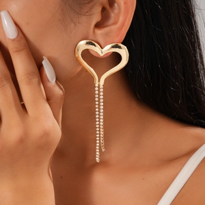 Close-up of gold oversized hollow heart earrings with long sparkling rhinestone tassels