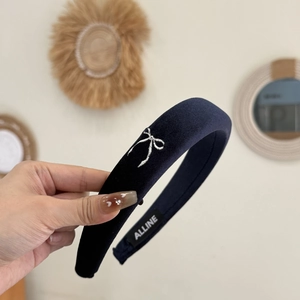 Detail of navy velvet padded headband featuring silver bow embroidery and brand label
