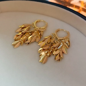 Macro detail of golden leaf tassel earrings featuring a textured metallic finish