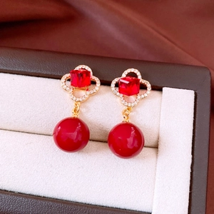 Macro detail of vintage gold flower earrings with red beads and zircon clover pendant