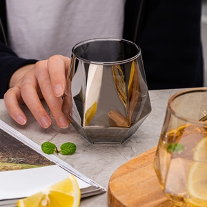 Detailed view of smoky grey hexagonal glass held by hand with lemon and mint garnish