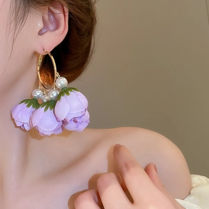 Detail of silk purple flower petal earrings with hanging pearls on a golden metal hoop