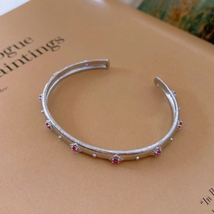 Close-up of silver-toned cuff bracelet with pink gemstones and brushed metal texture