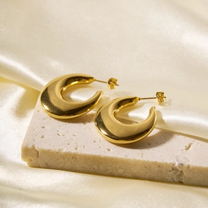 Detail of golden hollow C-shaped earrings on textured stone and cream silk fabric
