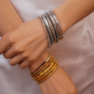 Macro shot of layered metallic bracelets with textured gold and silver finish on silk