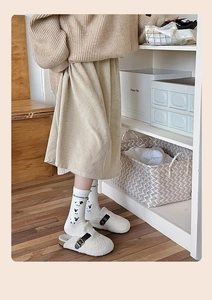 Détail de chaussettes en coton blanc à motif mouton et pantoufles en peluche beige