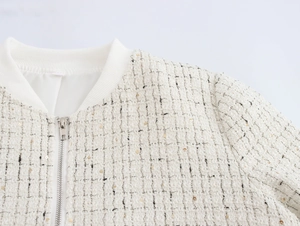 Détail de la veste en tweed blanc montrant des accents dorés et des poignets en maille