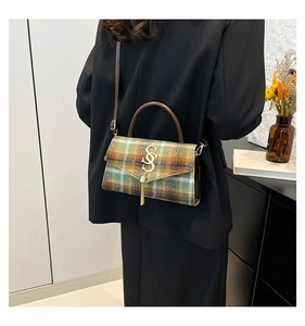 Detail of green plaid crossbody bag with gold metal tassel and vintage logo on black blazer