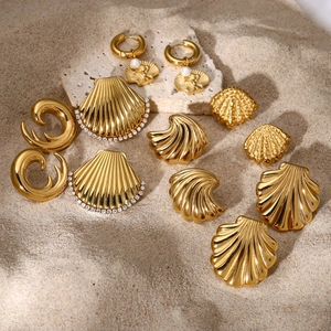 Golden shell earrings set with pearls and rhinestones on natural sand and stones