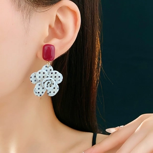 Détail d'un clou carré rouge et pendentif fleur à pois noirs porté par un mannequin
