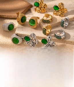 Close-up of gold titanium C-shaped flower earrings with emerald green zircon accents