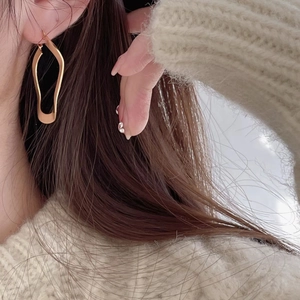 Close-up of minimalist irregular gold hoop earring worn by a model in soft lighting