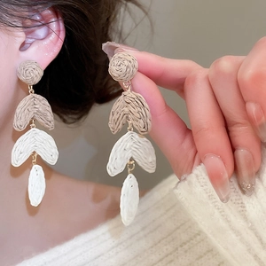 Detail of woven raffia tassel earrings in white and khaki on a fashion model