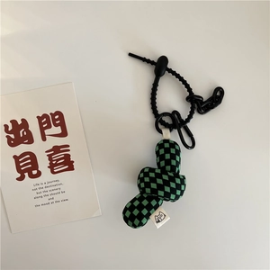 Macro detail of green and black checkerboard plush knot charm with spring cord and clip