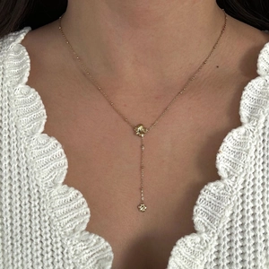 Close-up of gold Y-shaped necklace with flower pendant worn over a white sweater