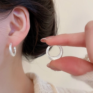 Close-up of minimalist brushed silver hoop earring held in fingers showing matte metal texture