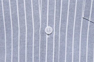 Macro shot of blue and white striped oxford fabric with white button detail on shirt