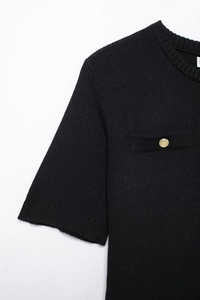 Detail of black knit top featuring round neck and pocket with golden button detail