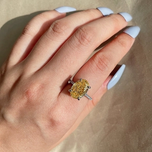 Detail of an oval yellow gemstone ring with pavé side stones on champagne satin fabric