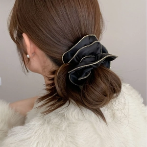 Chouchou en satin noir avec bordure chaîne dorée porté sur un chignon