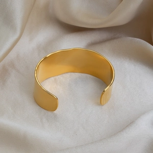 Détail macro du bracelet doré 18K à bords ondulés sur un tissu en soie douce