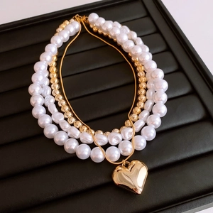 Close-up of layered pearl necklace with golden beads and a heart-shaped pendant