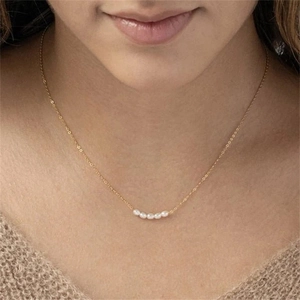 Close-up of a gold-plated necklace featuring four small white pearls on a delicate chain