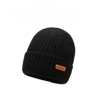 Detail of black winter beanie with ribbed texture and brown leather label with logo