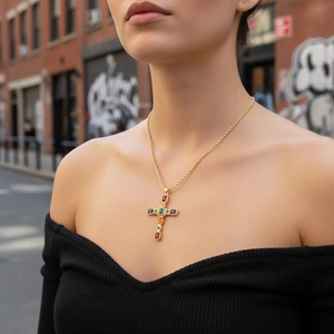 Dettaglio di una collana a croce placcata oro con zirconi colorati su un abito elegante