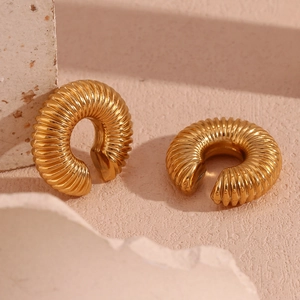 Close-up of golden hollow twisted earrings on a textured stone display surface