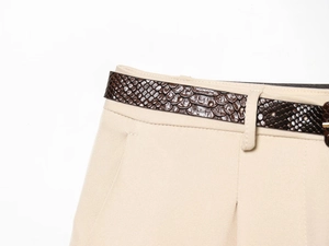 Détail d'un short beige avec une ceinture marron motif serpent sur fond blanc épuré