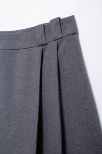 Close-up of waist belt loops and pleated grey skirt fabric detail on white background