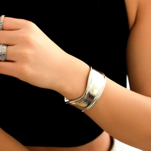Close-up of a wide silver wavy bangle and ring set showing polished mirror-like texture