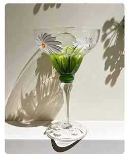 Detail of hand-painted daisy pattern on clear margarita glass with soft shadow